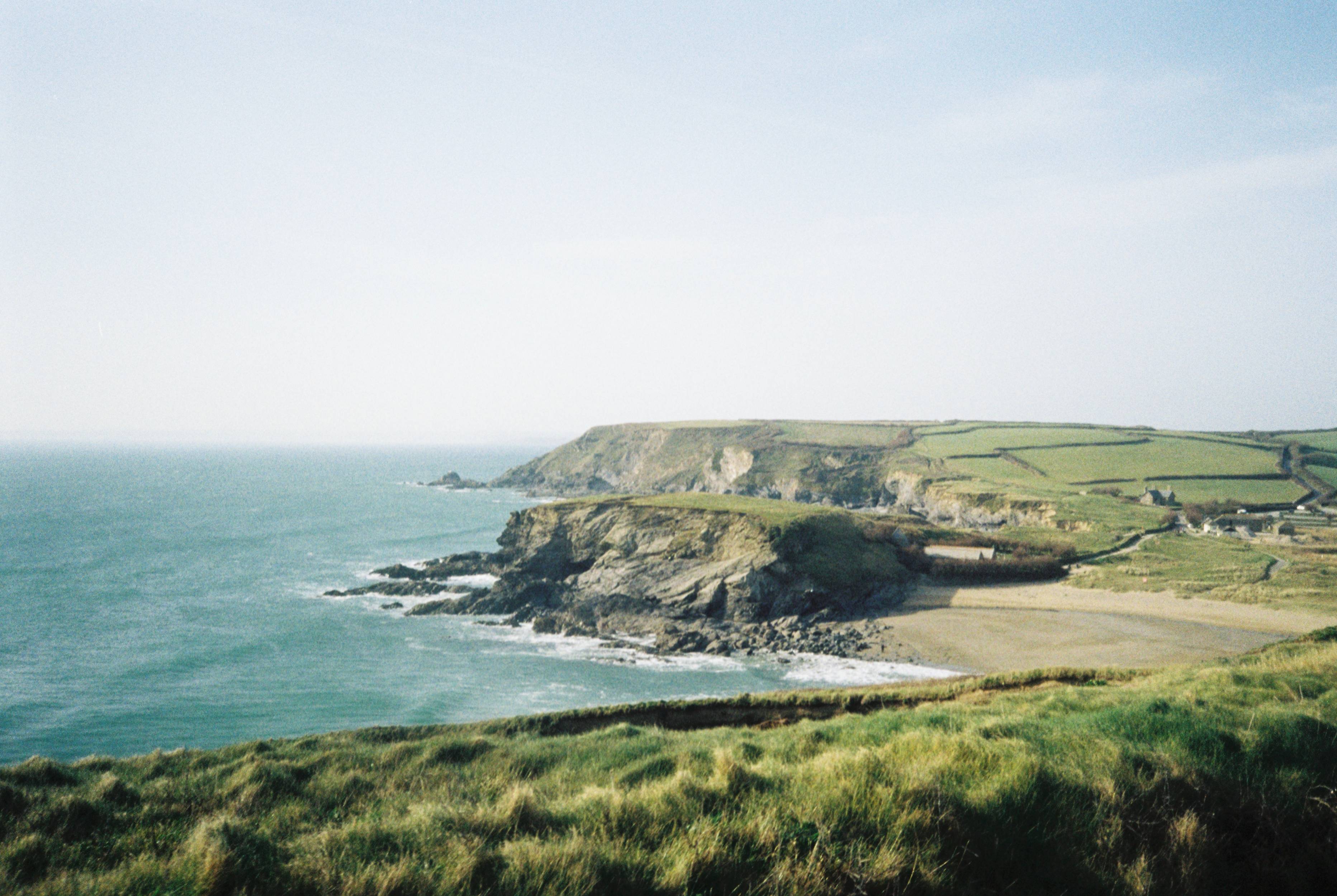 Landscape image shows the Cornish coastline; the cliffs in the background are set against the ocean